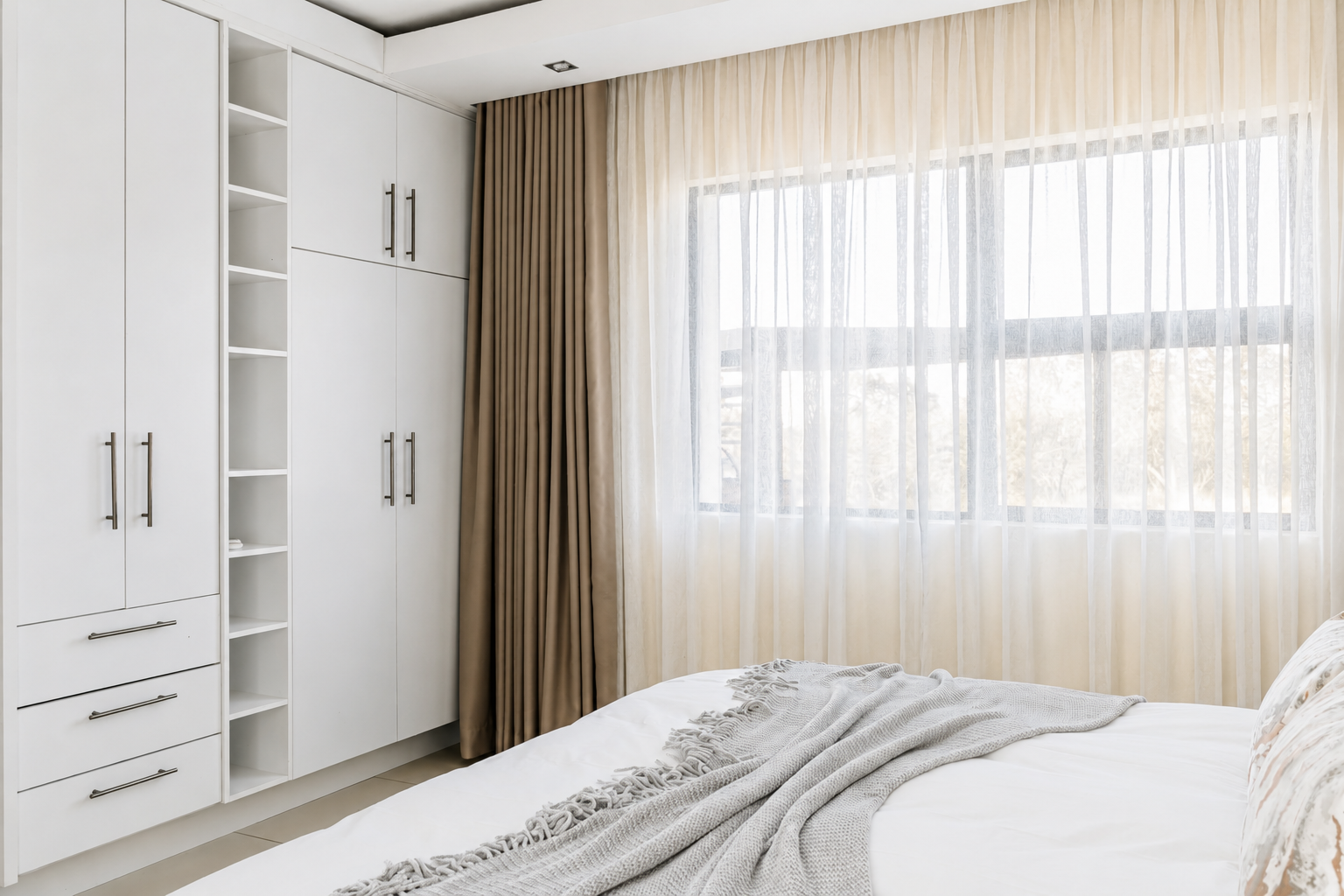 Bedroom with fitted white wardrobes and sheer curtains